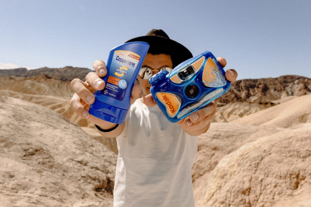 Young man holding sunscreen and disposable camera